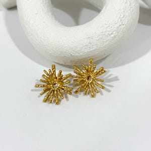 May include: A pair of gold starburst earrings with a textured finish.
