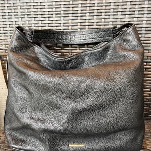 May include: Black leather hobo bag with a gold-toned logo on the front.