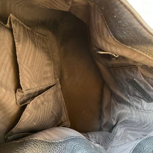 May include: The inside of a brown leather handbag with a zippered pocket and a brown patterned lining.