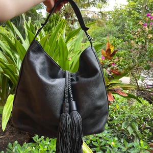 May include: Black leather hobo bag with a long tassel and braided rope handles.