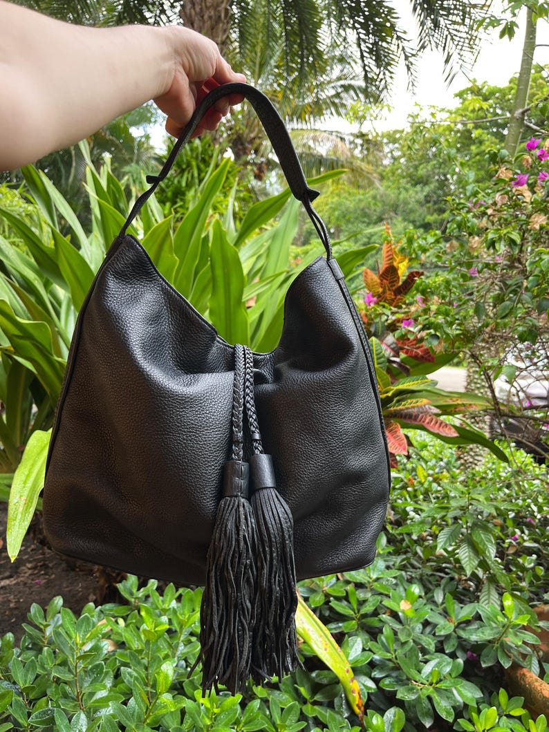 May include: Black leather hobo bag with a long tassel and braided rope handles.