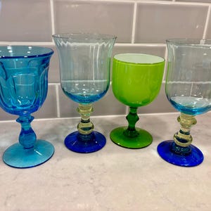 May include: Four colorful stemmed glasses. The glasses are in shades of blue and green. The bases are blue, and the stems are a mix of yellow and green. The glass on the far right has a wavy rim.