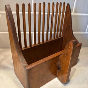 May include: A vintage wooden letter holder with a warm brown finish. The holder features a slatted back and a rectangular base, with a small side compartment. The design is simple and functional, suitable for organizing mail or documents.