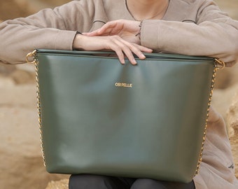 Pode incluir: Uma bolsa tote verde escura com uma alça de corrente dourada e o texto "OBI PELLE" em letras douradas.