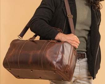 May include: A brown leather duffel bag with a long strap. The bag has a distressed look and is made of high-quality leather.