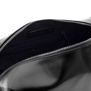May include: Black leather cosmetic bag with a silver zipper. The bag is open, revealing a dark interior with a small zippered pocket. The brand name is visible inside the bag.