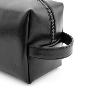 May include: A black leather toiletry bag with a silver zipper and a handle. The bag is square-shaped and features a small embossed logo on the front. The bag is designed for travel and personal care items.