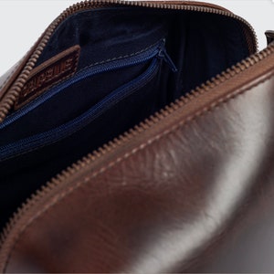 May include: Brown leather travel wash bag with a zip closure and a blue fabric lining. The bag has a small zipped pocket on the inside.