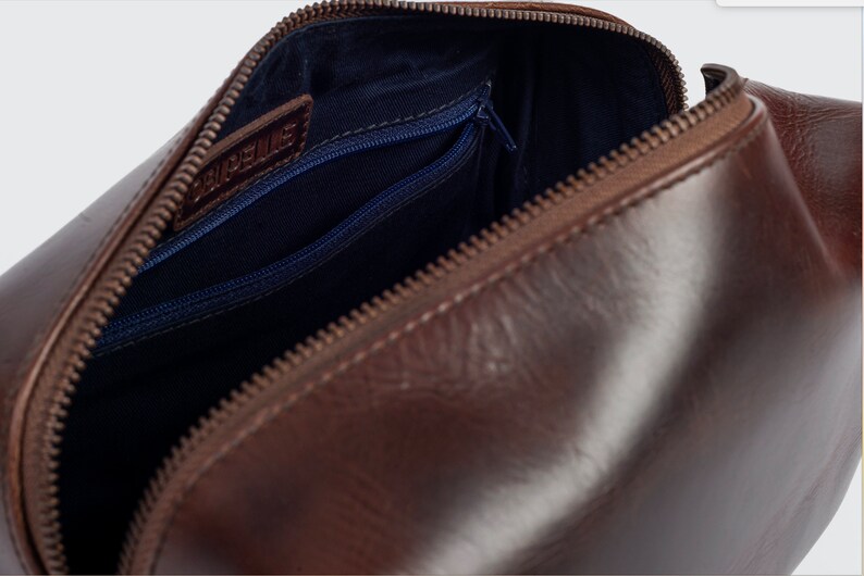 May include: Brown leather travel wash bag with a zip closure and a blue fabric lining. The bag has a small zipped pocket on the inside.