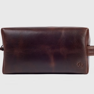 May include: A brown leather travel wash bag with a zip fastening and a leather handle.