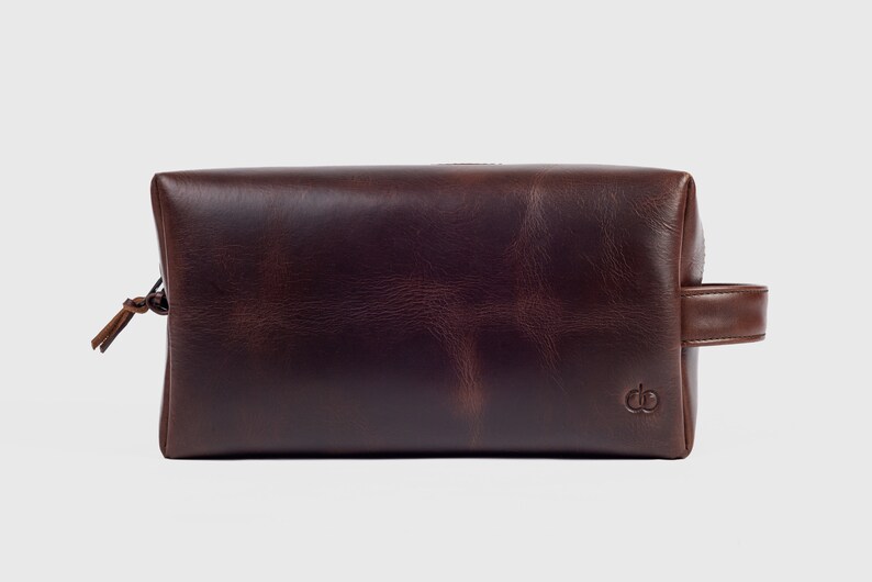 May include: A brown leather travel wash bag with a zip fastening and a leather handle.