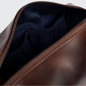 May include: A brown leather travel wash bag with a zip fastening and a blue fabric lining. The bag has a small pocket inside.