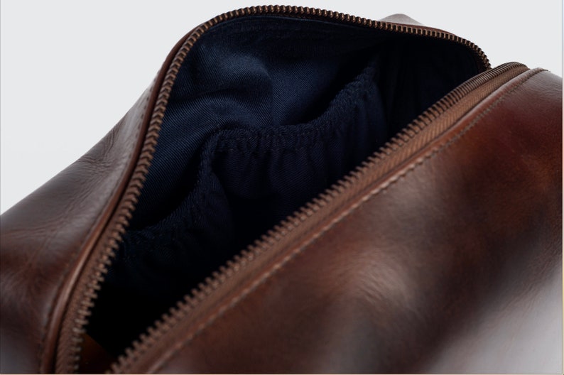 May include: A brown leather travel wash bag with a zip fastening and a blue fabric lining. The bag has a small pocket inside.