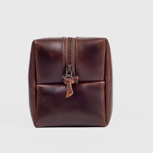 May include: A brown leather zippered wash bag with a brown leather zipper pull.