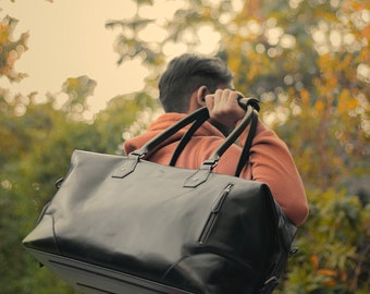 May include: A black leather duffel bag with a zipped pocket and a strap. The bag is being carried by a person wearing a burnt orange hoodie.