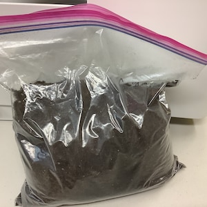 Peut inclure: Un sac en plastique transparent avec une fermeture éclair rose rempli de terreau brun foncé.