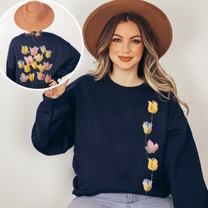 Peut inclure: Un sweat-shirt bleu marine avec une ligne verticale de tulipes color&eacute;es imprim&eacute;es sur le devant. Le sweat-shirt a un col rond et des manches longues.