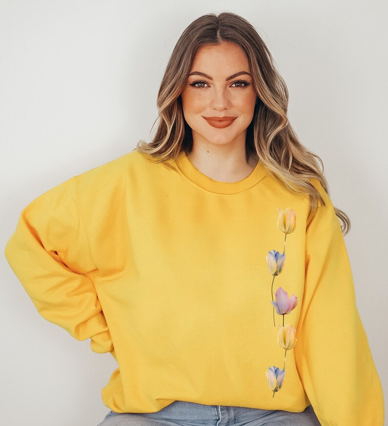 Peut inclure: Un sweat-shirt jaune avec une rang&eacute;e verticale de tulipes de style aquarelle dans des tons de rose, bleu et jaune sur le c&ocirc;t&eacute; droit.