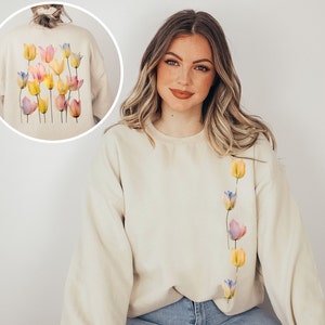 Peut inclure: Un sweat-shirt cr&egrave;me avec une ligne verticale de tulipes aquarelle dans des tons de rose, jaune et bleu sur le c&ocirc;t&eacute; gauche de la poitrine.