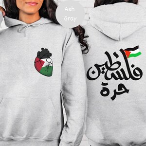 Może przedstawiać: Szara bluza z kapturem z sercem z flagą palestyńską z przodu i arabskim tekstem "فلسطين حرة" (Palestyna jest wolna) z flagą palestyńską z tyłu.