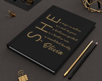 May include: A black journal with gold lettering that reads "SHE is magic in motion, is a soul of grace, is brilliance sparked, is a heart so rare, is unmatched beauty, Olivia." Gold pencils and paper clips are also visible.