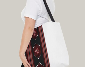May include: A white tote bag with a black and red geometric pattern on the side. The pattern features a repeating diamond shape with white and red accents.