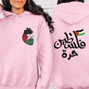 Może przedstawiać: R&oacute;żowa bluza z sercem w kształcie palestyńskiej flagi z przodu i arabskim napisem "Palestyna" z palestyńską flagą z tyłu.