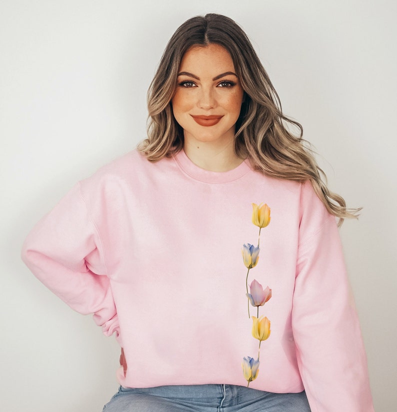 Peut inclure: Un sweat-shirt rose avec une ligne verticale de tulipes aquarelle dans des tons de jaune, bleu et violet.