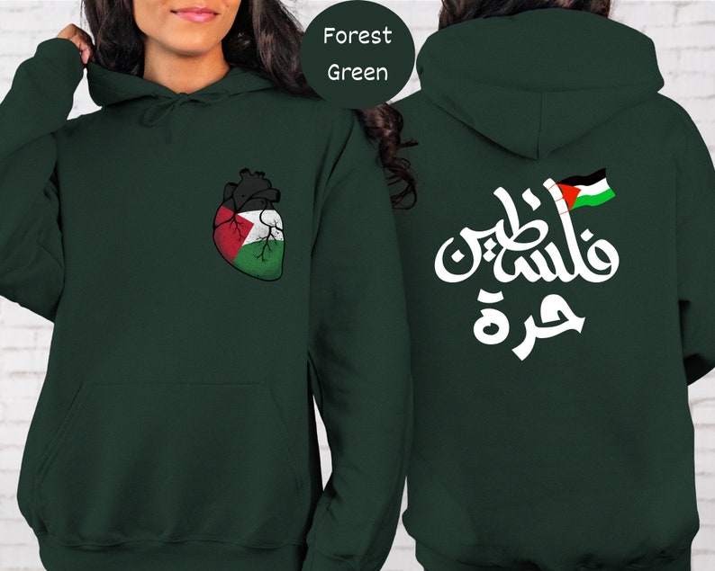 Może przedstawiać: Zielona bluza z kapturem w kolorze leśnym z białym arabskim napisem i flagą palestyńską z tyłu. Prz&oacute;d zdobi serce w kolorach palestyńskiej flagi.