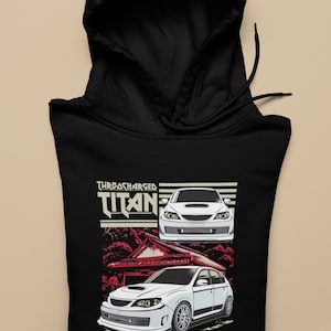May include: Black hoodie featuring a white Subaru Impreza WRX STI printed on the front. The car is surrounded by a red and white Japanese-inspired design. The text "TURBOCHARGED TITAN" is printed above the car.