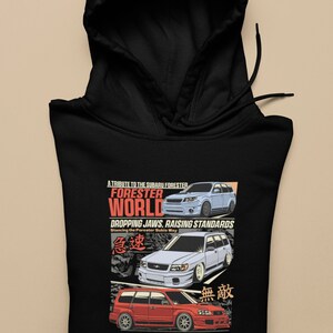 Peut inclure: Sweat-shirt à capuche noir avec un imprimé graphique de trois Subaru Forester. Le texte sur le graphique est "A Tribute to the Subaru Forester", "Forester World", "Dropping Jaws, Raising Standards", "Stancing the Forester Subie Way", "Turn Heads, Take Risks: Discover the World of Stanced Subies", et comprend des caractères japonais.