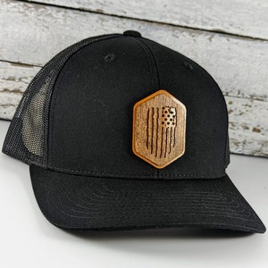 May include: A black trucker hat with a mesh back and a wooden American flag patch.
