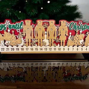 May include: A wooden Christmas advent calendar with a red and white design. The calendar features the words "Days until Christmas" in green script, along with wooden nutcrackers, Christmas trees, and numbered days.
