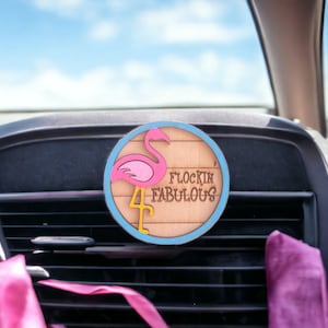 May include: Pink flamingo car air freshener with the text "Flockin' Fabulous" on a wooden background.