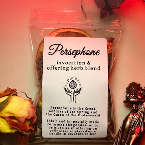 May include: A small, clear plastic bag filled with dried herbs and flowers. The bag has a white label with the text "Persephone invocation & offering herb blend" and a small black and white symbol. The label also includes a description of Persephone, the Greek Goddess of the Spring and the Queen of the Underworld.