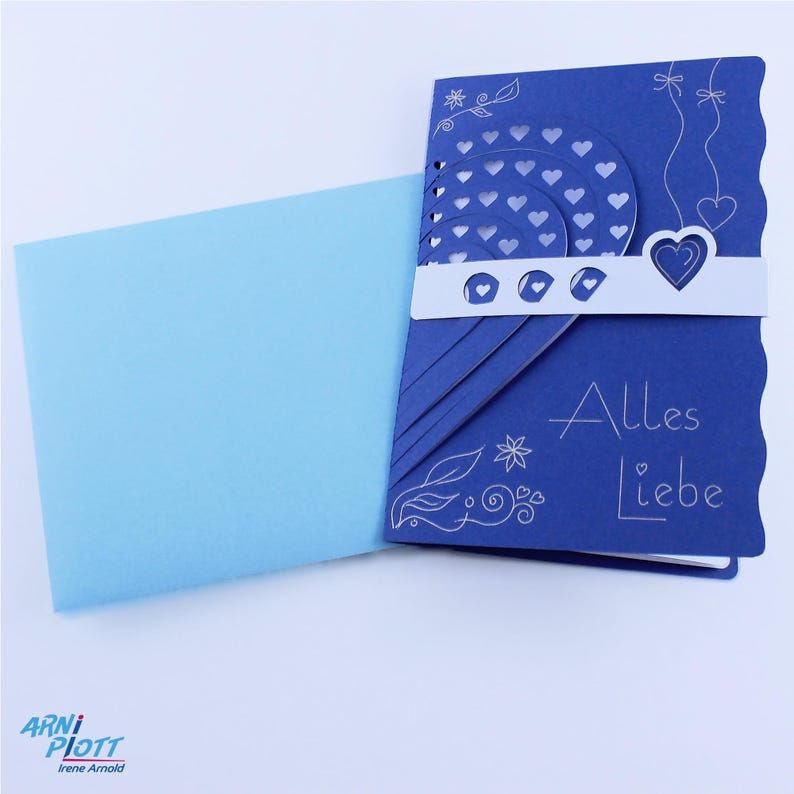 May include: A blue card with a white heart and the words "Alles Liebe" in white lettering. The card is folded in half and has a light blue envelope.