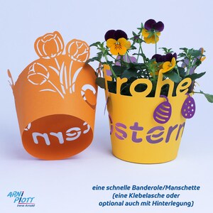 Op de afbeelding: Twee papieren bloempotbedekkingen, een oranje met een wit tulpenontwerp en de tekst "mrs" en een gele met een paars "Frohe Ostern" (Gelukkig Pasen) ontwerp.