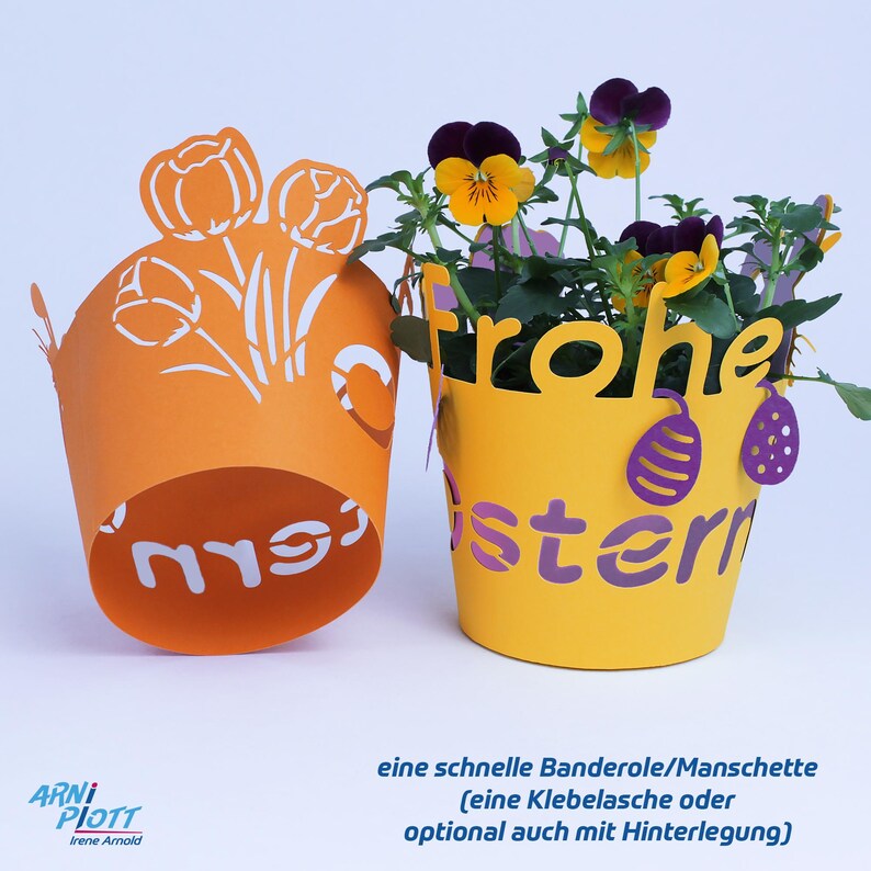 Op de afbeelding: Twee papieren bloempotbedekkingen, een oranje met een wit tulpenontwerp en de tekst "mrs" en een gele met een paars "Frohe Ostern" (Gelukkig Pasen) ontwerp.