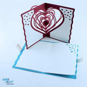May include: A burgundy pop-up card with a 3D heart design. The card is open and the heart is fully extended. The card is decorated with small white hearts.