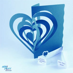 May include: A blue paper heart card with a pop-up design. The card has a scalloped edge and the text "Streifen umklappen und..." and "vom Herz l&ouml;sen" on the front.