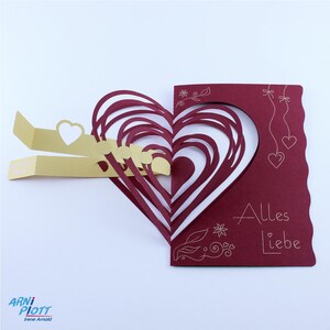 May include: A red card with a pop-up heart design. The heart is made of multiple layers of red paper. The card has the text "Alles Liebe" written on it in white.