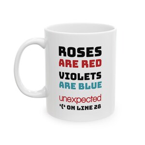 May include: White ceramic mug with a curved handle. The mug features the text "ROSES ARE RED, VIOLETS ARE BLUE, unexpected, 'ON LINE 28" in black, red, and blue lettering. The mug is designed for hot or cold beverages.