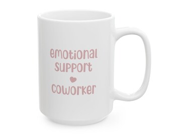 May include: White ceramic mug with the text "emotional SUPPORT coworker" in a soft pink font. A small pink heart is between the words "SUPPORT" and "coworker". The mug has a large handle.