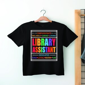 May include: Black t-shirt with a rainbow graphic that says "Library Assistant". The graphic is surrounded by a white box and includes the words "Compassionate", "Reliable", "Caring", "Loving", "Dedicated", "Kind", "Loyal", "Warm", and "Fun".