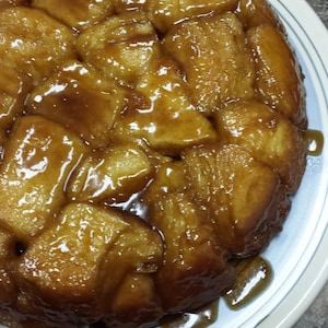 May include: A close-up of a round, golden-brown dessert, possibly monkey bread, on a white plate with blue stripes. The pastry is covered in a glossy, caramel-like sauce, with some sauce drizzled on the plate.