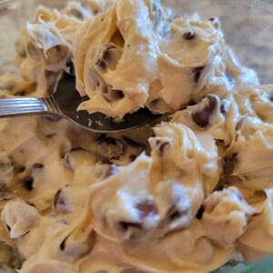 May include: A close-up of a bowl of cookie dough with chocolate chips. The dough is light brown and creamy, and the chips are dark brown.