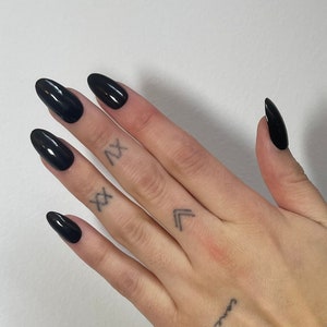 May include: A hand with black almond-shaped nails, featuring a small tattoo of a rose and a musical note on the wrist.