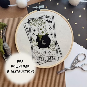 Pu&ograve; includere: Un telaio da ricamo con un disegno di carta dei tarocchi raffigurante un calderone nero con liquido verde gorgogliante, un pipistrello e stelle. Il testo "THE CAULDRON" &egrave; sotto l'immagine. Sono visibili anche le parole "PDF DOWNLOAD & INSTRUCTIONS".