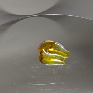 Può includere: Un anello di vetro giallo con un design curvo unico. L'anello è fatto di vetro trasparente con una tinta gialla.
