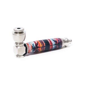 May include: A silver metal smoking pipe with a colorful design featuring a sunset and palm trees. The pipe has a round bowl and a long, cylindrical stem.